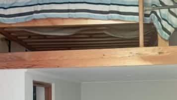 Une chambre avec un lit superposé, une porte et un lit simple recouvert d’une couverture bleue.