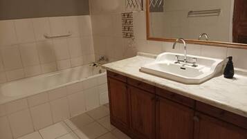 Un baño con bañera, lavamanos, armarios de madera y espejo.