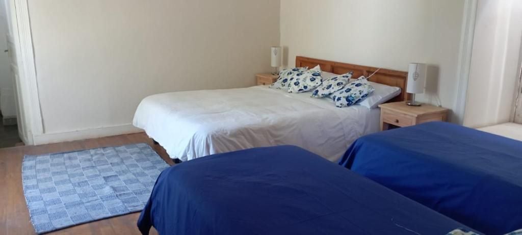 Un dormitorio con dos camas, una mesita de noche, una lámpara y una alfombra estampada.