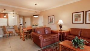 Uma sala de estar com sofá de couro marrom, mesa de centro de madeira e área de jantar com mesa e cadeiras.