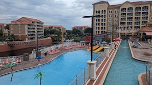 Una piscina grande con un tobogán de agua, rodeada de edificios con balcones y un cielo despejado.