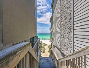 A narrow wooden pathway leading to a beach with a clear view of the ocean and a stone wall on one side. - Miramar Beach Villa 112 (Miramar Beach)