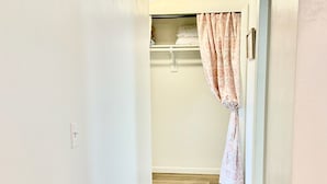 Un pasillo estrecho con suelo de madera que conduce a una habitación con una puerta blanca y una cortina rosa.