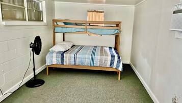Uma cama beliche com colcha listrada, um ventilador e uma janela com cortinas.