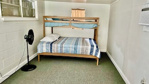 A bunk bed with a striped bedspread, a fan, and a window with curtains.