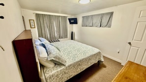 A bedroom with a bed, a wardrobe, a television, and a window with curtains.