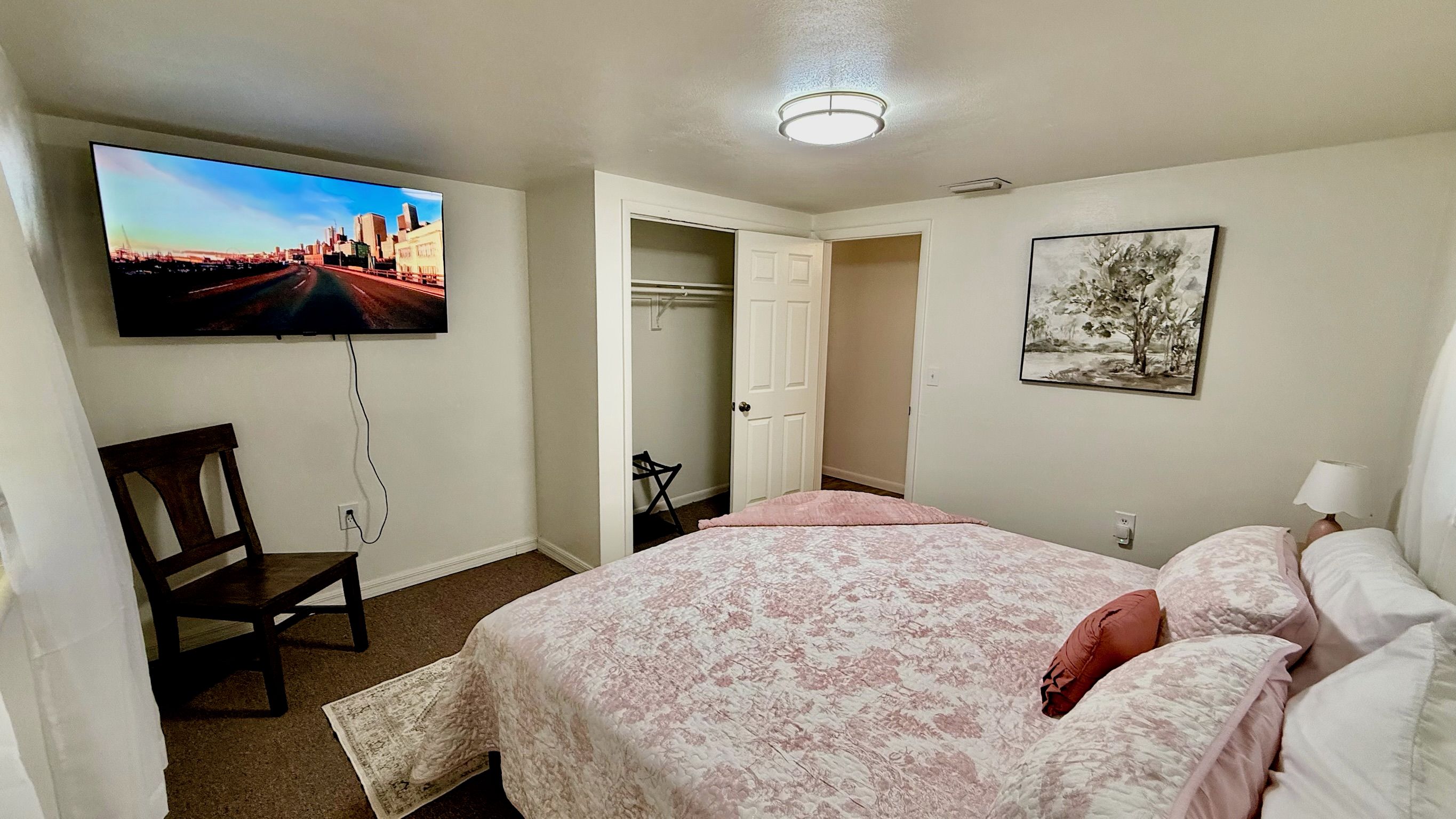 Quarto com cama, cadeira, televisão, armário e um quadro na parede.