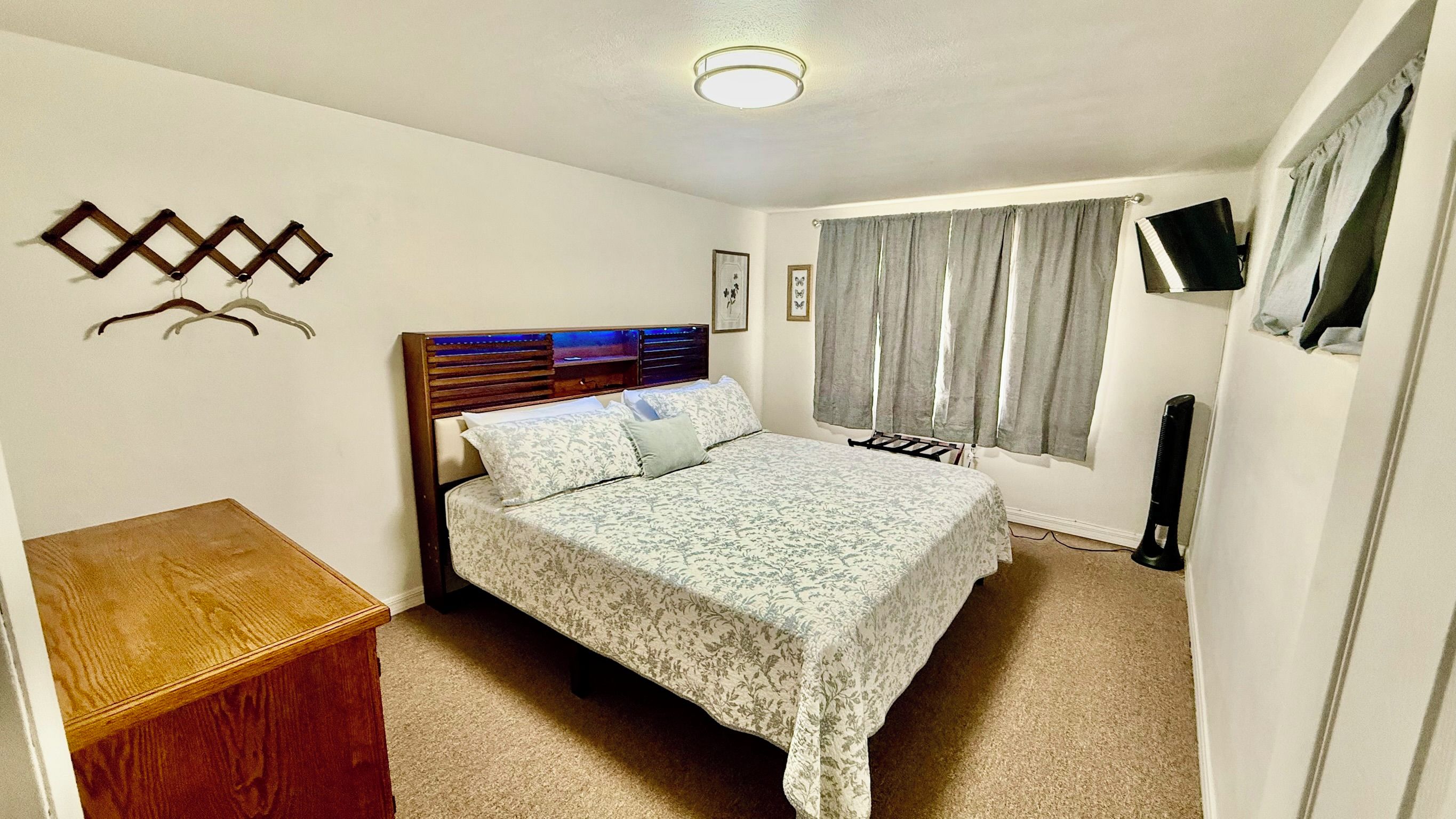 Una camera da letto con un letto, un comodino in legno, una televisione e una finestra con tende.