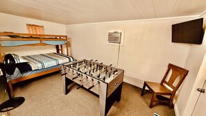 Ein Zimmer mit einem Etagenbett, einem Kicker, einem Sessel und einem an der Wand befestigten Fernseher.