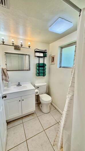Ein Badezimmer mit Toilette, Waschbecken und Spiegel. Ein Handtuchhalter mit Handtüchern sowie ein Fenster mit Blick.