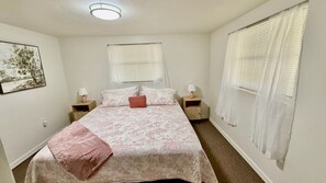 Ein Schlafzimmer mit einem Bett, zwei Nachttischen, einem Fenster mit Jalousien und einer Deckenleuchte.
