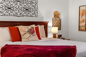 Une chambre d’hôtel avec un lit, des oreillers, un plaid rouge, une table de chevet avec une lampe et des œuvres d’art accrochées aux murs.
