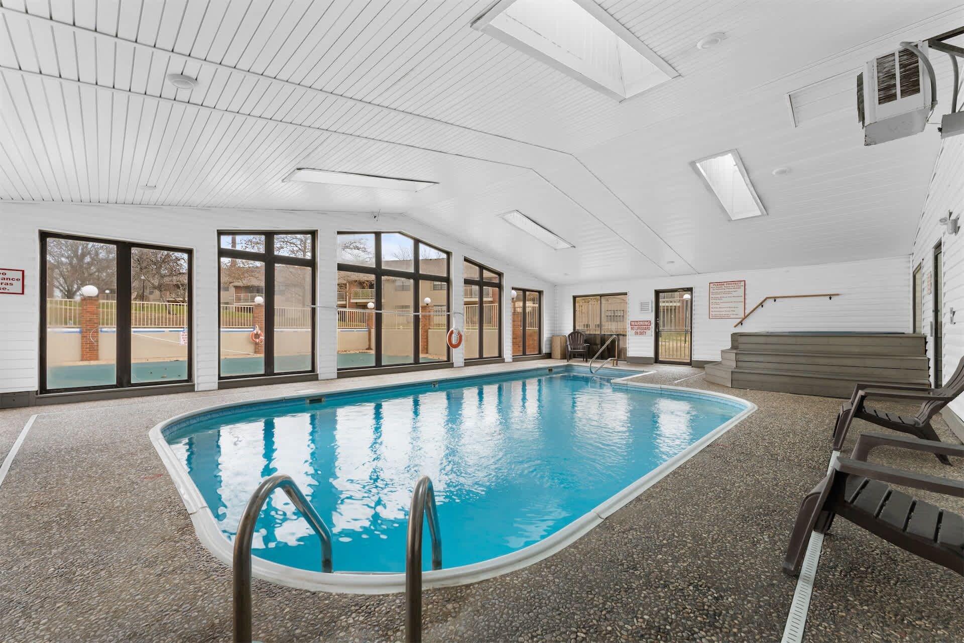 Una piscina interior con paredes de vidrio transparente, una silla de salvavidas y una escalera de piscina.