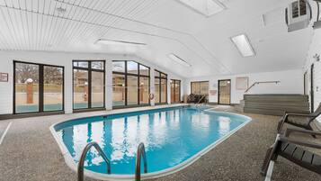 Una piscina interior con paredes de vidrio transparente, una silla de salvavidas y una escalera de piscina.