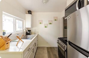Eine moderne Küche mit einem Edelstahl-Kühlschrank, einem Herd und einer Spüle. Auf der Arbeitsfläche liegen Holzkochlöffel und ein Fenster sorgt für natürliches Licht.