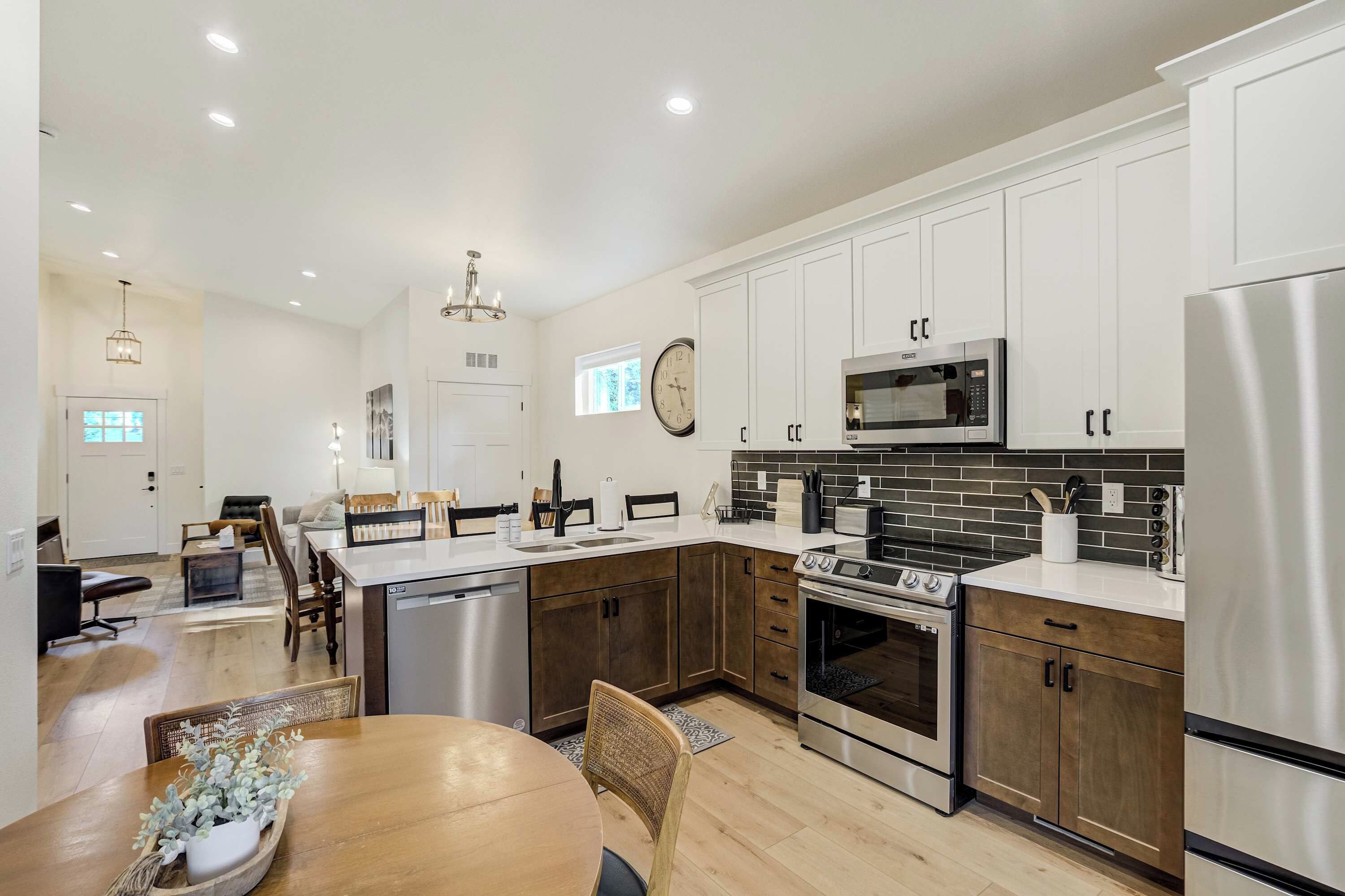 A modern kitchen with white cabinets, stainless steel appliances, and a dining area with a wooden table and chairs.