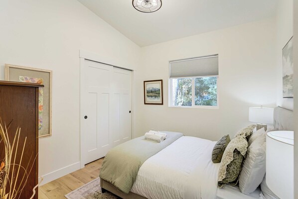 A bedroom with a bed, a window with blinds, a door, and a bedside table with a lamp.