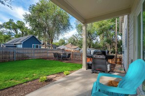 A backyard with a grill, a covered patio area, and a blue chair.