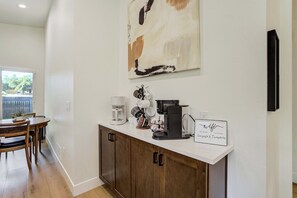 Una cocina con cafetera, un cartel con detalles de wifi y una zona de comedor con mesa y sillas.