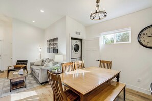 A living room with a sofa, a dining table with chairs, a chandelier, a clock, and a washing machine. - Golden Grove! Large Yard w/ Hot Tub Near Downtown (Colorado Springs)