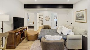 A modern living room with a television, sofa, ottoman, and a wooden cabinet. - Golden Grove! Large Yard w/ Hot Tub Near Downtown (Colorado Springs)