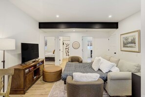 A modern living room with a television, sofa, ottoman, and a wooden cabinet. - Golden Grove! Large Yard w/ Hot Tub Near Downtown (Colorado Springs)