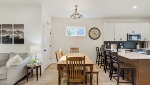 A modern kitchen with white cabinets, a built-in microwave, and a dining area with wooden chairs and a table. - Golden Grove! Large Yard w/ Hot Tub Near Downtown (Colorado Springs)
