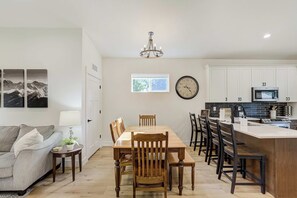 A modern kitchen with white cabinets, a built-in microwave, and a dining area with wooden chairs and a table. - Golden Grove! Large Yard w/ Hot Tub Near Downtown (Colorado Springs)