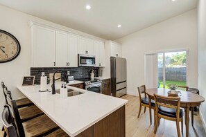A modern kitchen with white cabinets, a stainless steel refrigerator, a microwave, and a large island with a sink. - Golden Grove! Large Yard w/ Hot Tub Near Downtown (Colorado Springs)