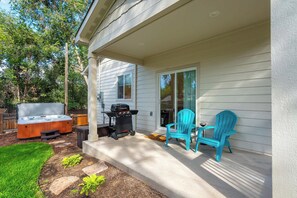 A covered patio with a grill, outdoor seating, and a hot tub.