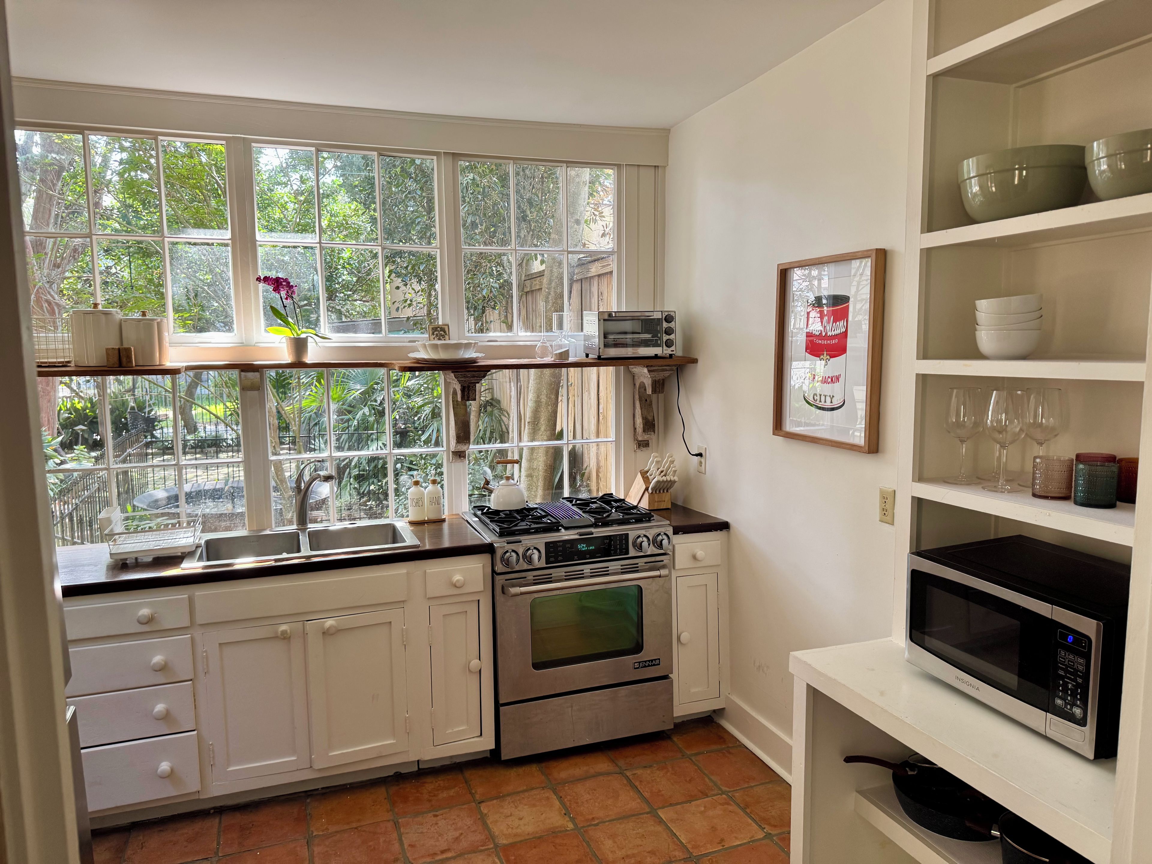 Une cuisine avec des meubles blancs, une cuisinière à gaz, un four, un four à micro-ondes et une fenêtre donnant sur un paysage verdoyant.