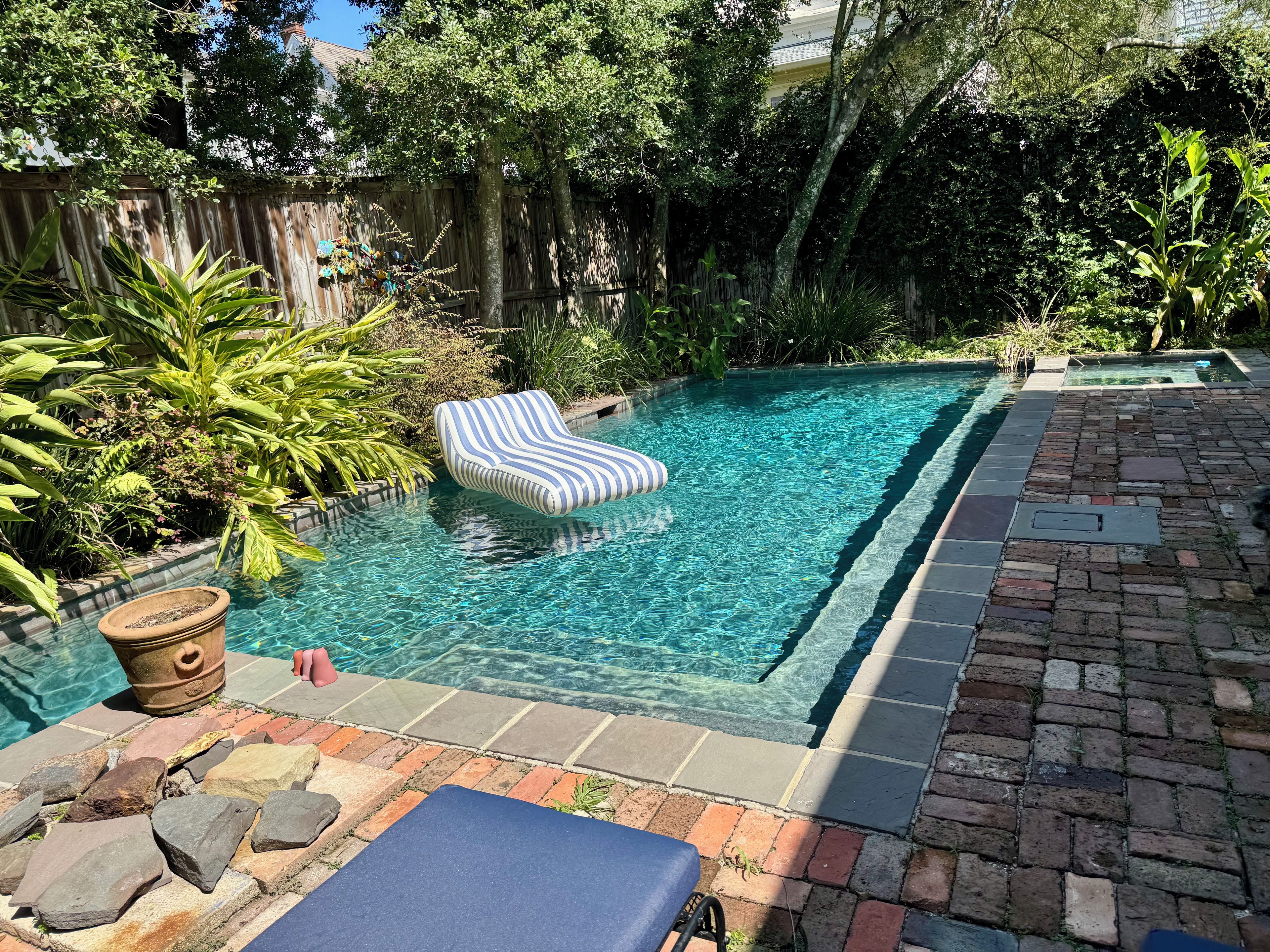 Une piscine avec un fauteuil de relaxation, entourée de plantes et d’une clôture en bois.
