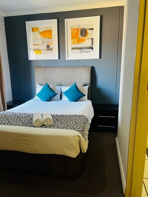 Une chambre d’hôtel avec un lit, deux tableaux abstraits encadrés, une tête de lit et une paire de serviettes enroulées posées sur le lit.