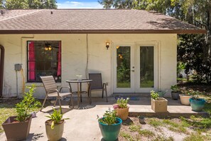 A single-story house with a patio area, a dining table, two chairs, and several potted plants. - Cozy 2BR Condo Near Beach & Ponce Inlet (Port Orange)