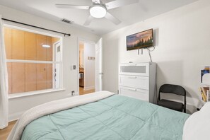 A bedroom with a bed, a ceiling fan, a TV, and a wardrobe. - Cozy 2BR Condo Near Beach & Ponce Inlet (Port Orange)