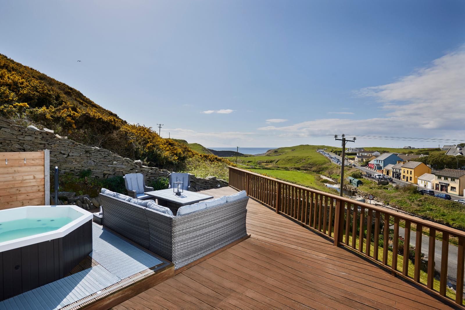 A wooden deck with a hot tub and seating area overlooking a coastal town.