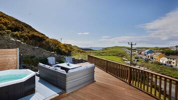 A wooden deck with a hot tub and seating area overlooking a coastal town.