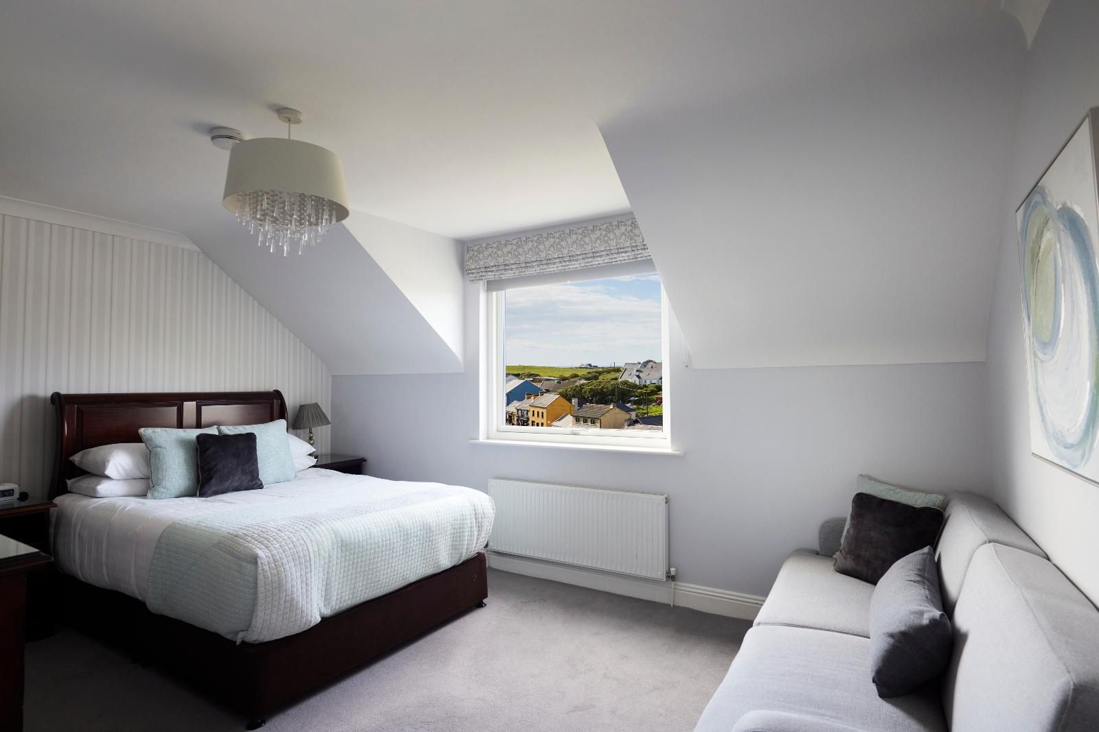 A bedroom with a large bed, a nightstand, a window with a view, a radiator, and a ceiling light fixture.