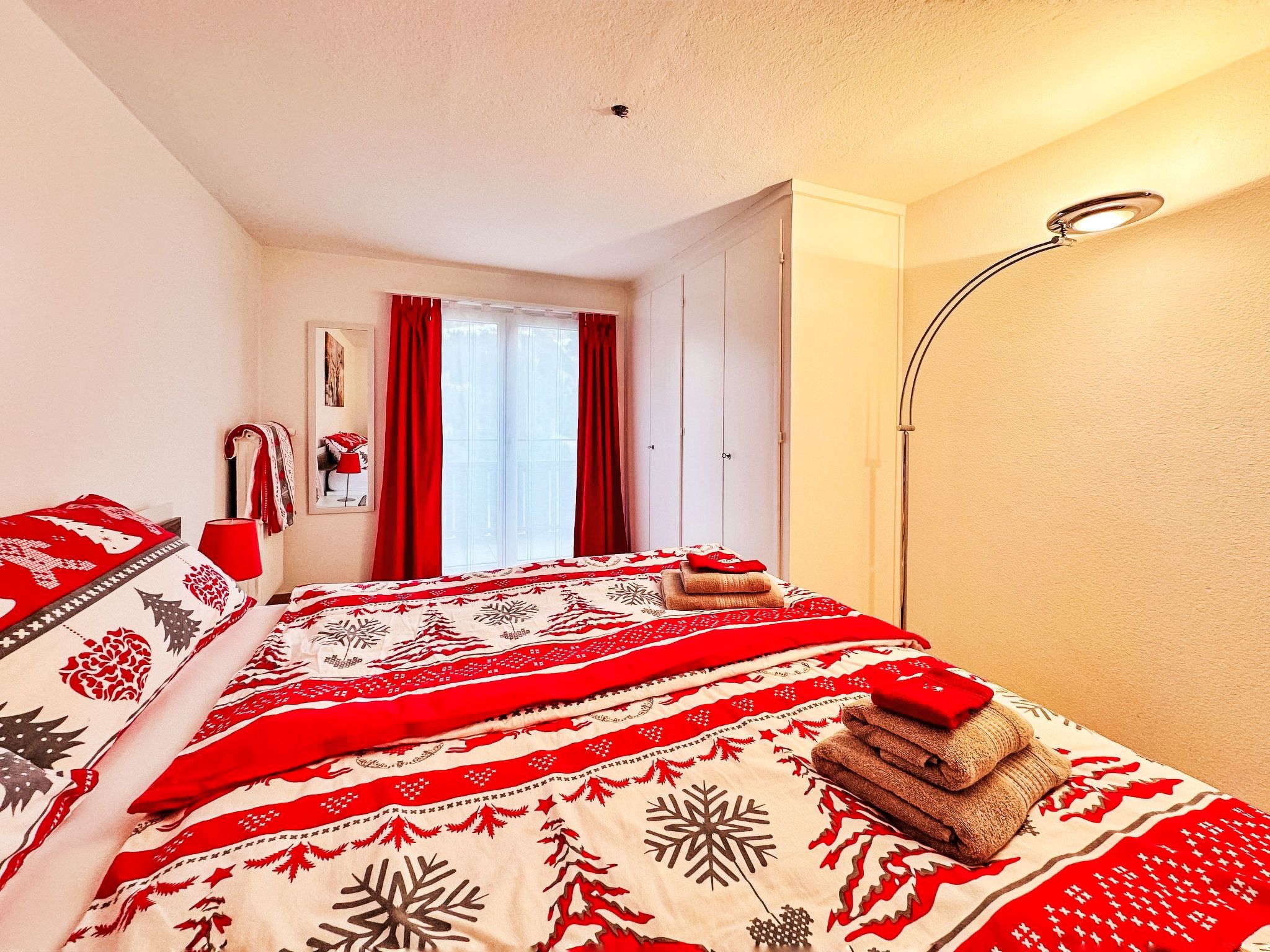 A bedroom with a bed, red curtains, a bedside lamp, and a window.