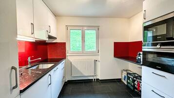 Una cocina con armarios blancos, encimera roja, horno Siemens y ventana con vistas.