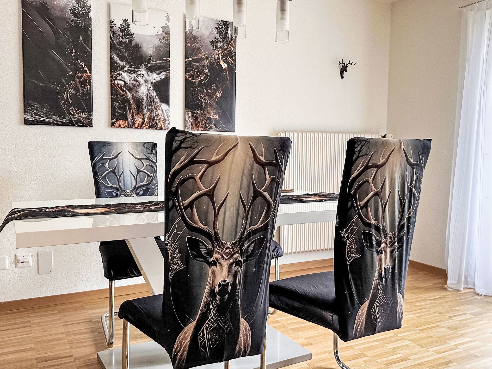 Zona pranzo con tavolo bianco, sedie nere con decorazioni a cervo e opere d'arte alle pareti.