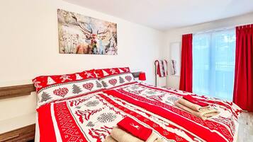 A hotel room with a large bed, a painting on the wall, and a window with red curtains.