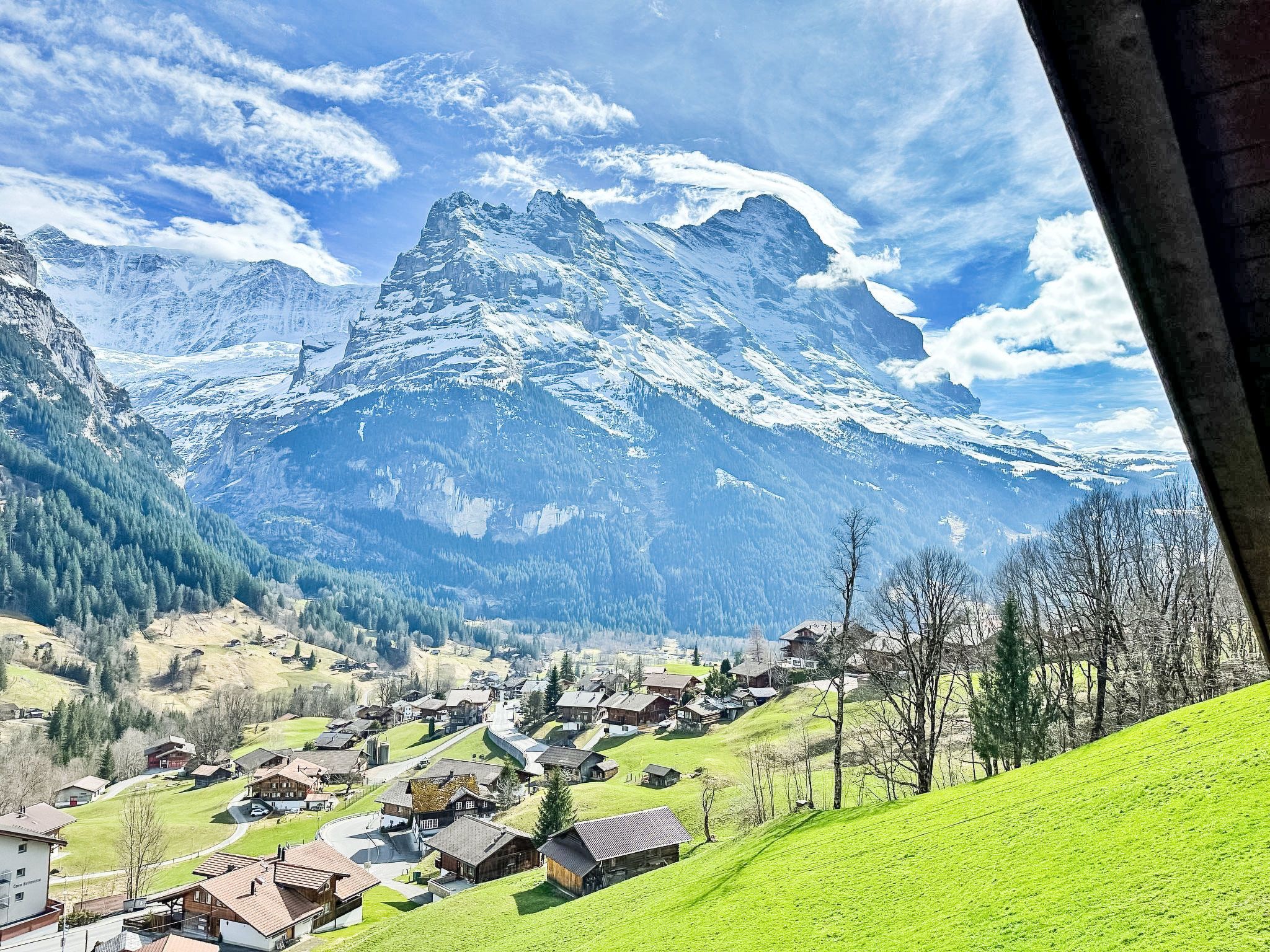Ein Bergdorf mit traditionellen Häusern, blauem Himmel und schneebedeckten Berggipfeln im Hintergrund.