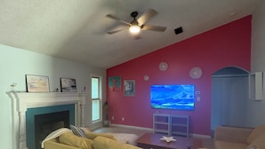Ein Wohnzimmer mit beiger Couch, Kamin, Fernseher und Deckenventilator.