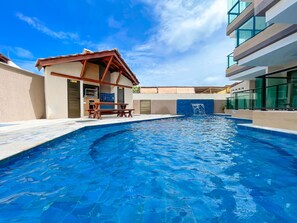 A swimming pool with a wooden deck and a small pavilion, surrounded by modern buildings. - Tangaroa #106 - Comfortable Apartment by Carpediem (Ipojuca)