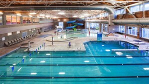 Ein Hallenbad mit mehreren Bahnen, einer Wasserrutsche und Liegestühlen.