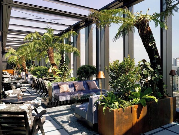 Eine moderne Rooftop-Lounge mit Glasdach, Sitzgelegenheiten im Freien und üppiger Bepflanzung.