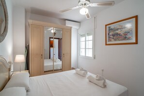 A hotel room with a bed, a wardrobe, a ceiling fan, a window, and a painting on the wall. - Apartment in Nerja Near Torrecilla Beach (Nerja)