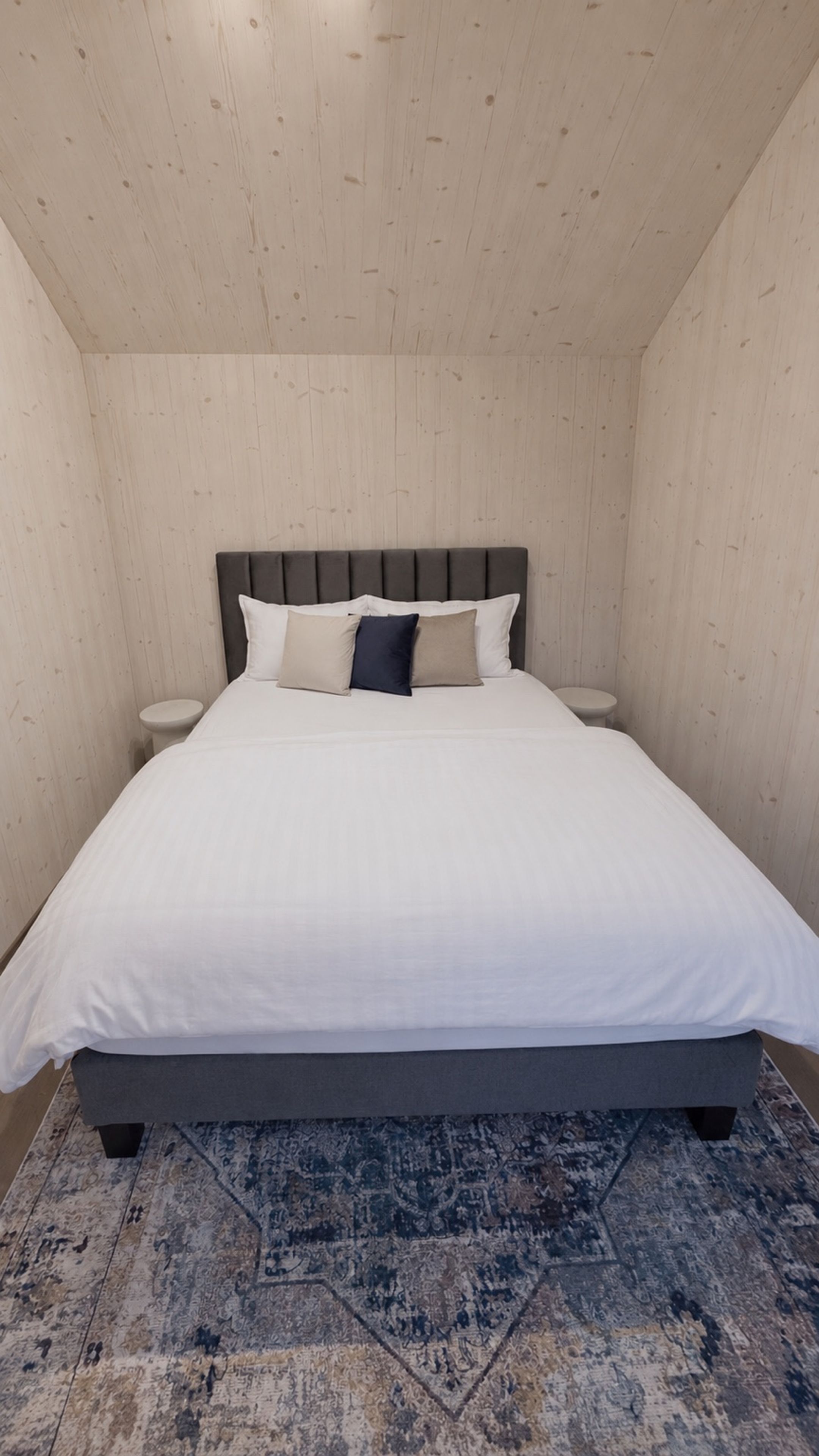 A bedroom with a bed, two bedside tables, and a patterned rug.