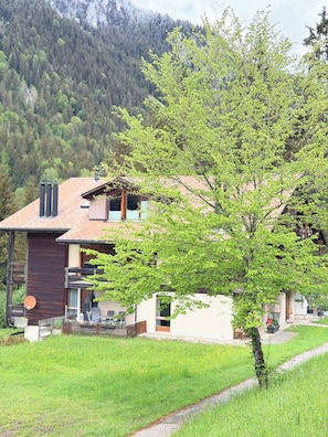 Una casa de dos pisos con techo inclinado, chimenea y balcón.